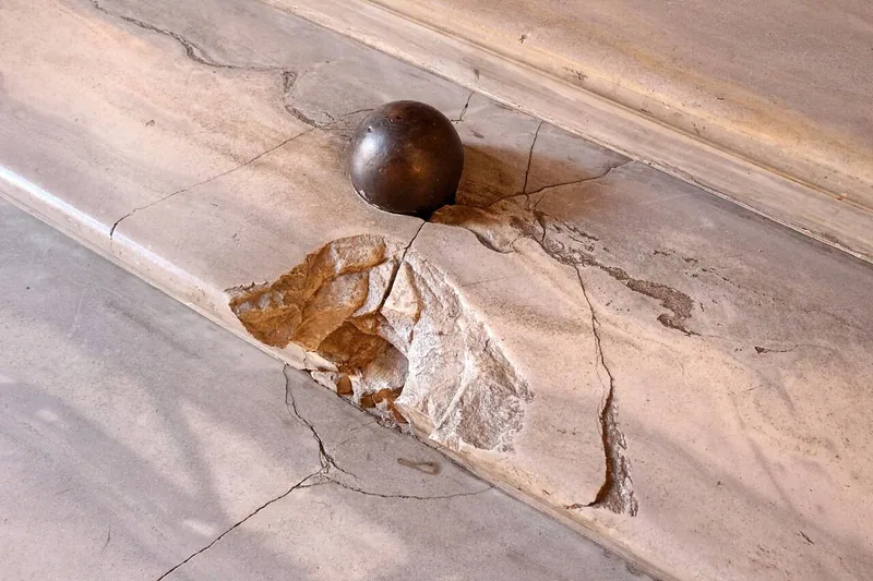 An iron cannonball resting in a shattered step of white marble