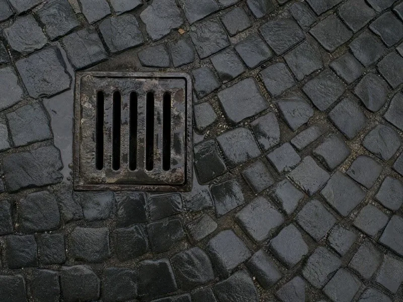 Wet sampietrini cobbles and an iron drain grate after rain